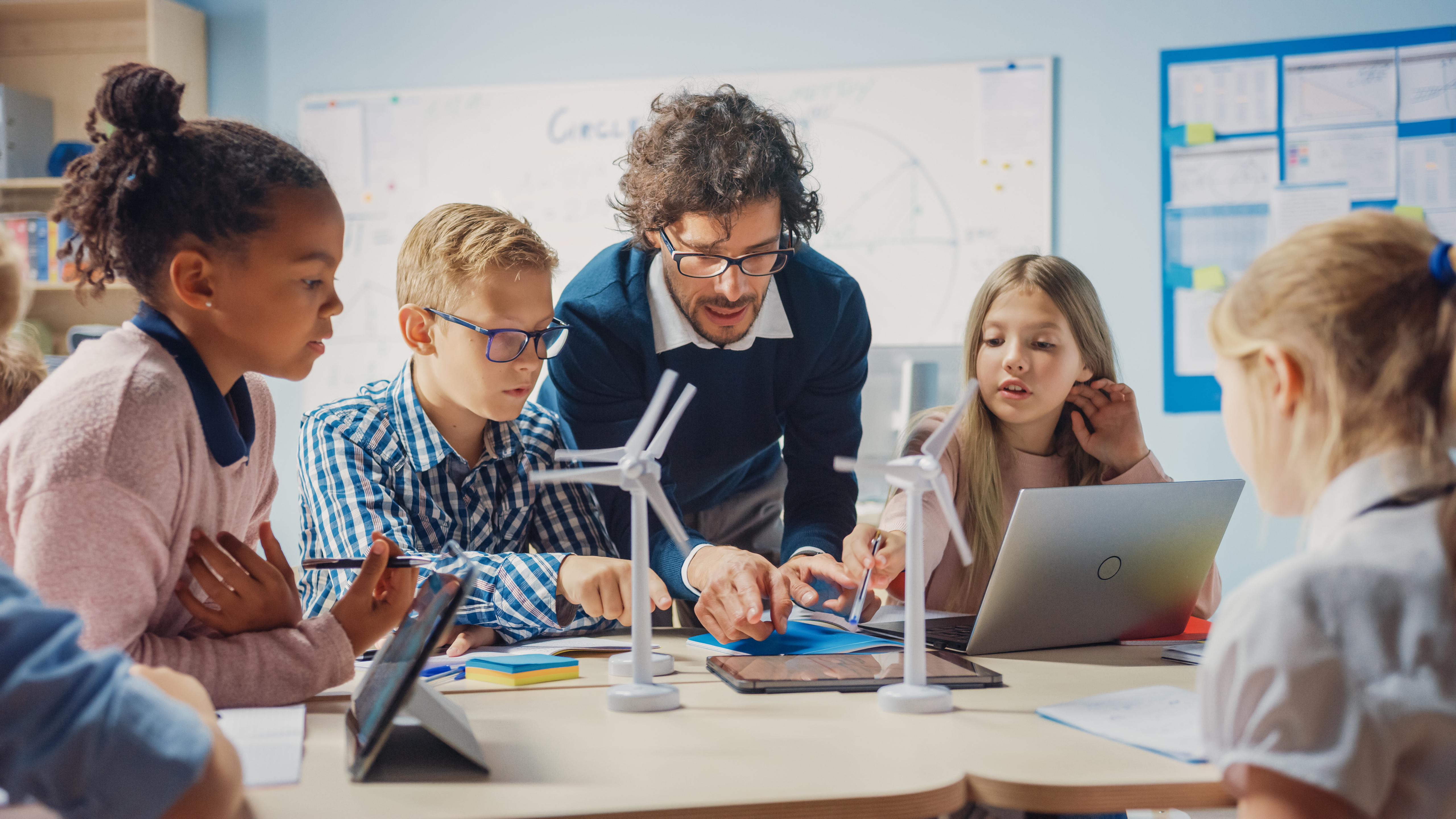 A teaching assistant helping young students working on small wind turbines at a table.